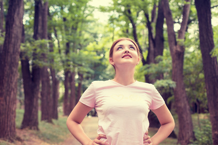 Portrait young attractive smiling fit woman resting after workout sport exercises outdoor looking up enjoying fresh air standing on background park trees.の写真素材