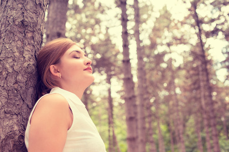 Side profile portrait relaxing young woman enjoying summer day in forest taking deep breath leaning on a treeの写真素材