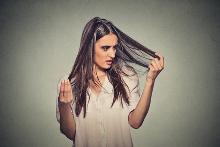 Closeup unhappy frustrated young woman surprised she is losing hair, receding hairline. Gray background. Human face expression emotion. Beauty hairstyle conceptの写真素材