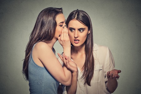 Girl whispering into woman ear telling her something funny and shocking secret. Human communication emotions facial expression feelingsの写真素材