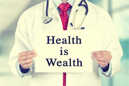Closeup doctor hands holding white card sign with health is wealth text message isolated on hospital clinic office background.の写真素材