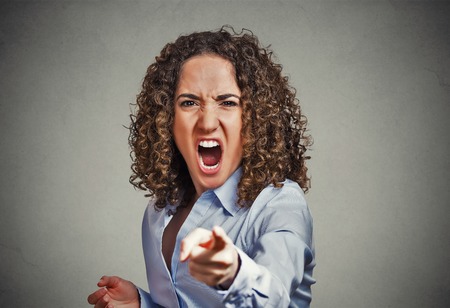Portrait angry young woman pointing finger at camera screaming isolated on grey wall backgroundの写真素材