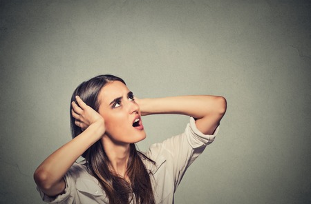Portrait young annoyed, unhappy, stressed woman covering her ears, looking up, to say, stop making loud noise, giving me headache isolated grey background with copy space. Negative emotion reactionの写真素材