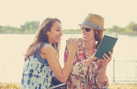 Two friends happy students women studying reading book outdoors on summer sunny dayの写真素材