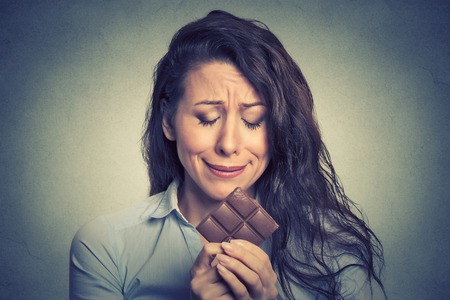 Portrait sad young woman tired of diet restrictions craving sweets chocolate isolated on gray wall background. Human face expression emotion. Nutrition concept. Feelings of guiltの写真素材
