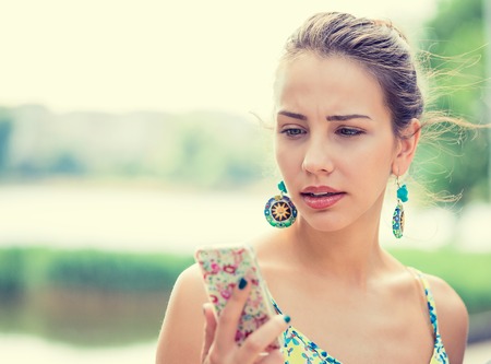 Closeup portrait upset sad skeptical unhappy serious woman talking texting on phone displeased with conversation isolated park outdoors background. Negative human emotion face expression feelingの写真素材