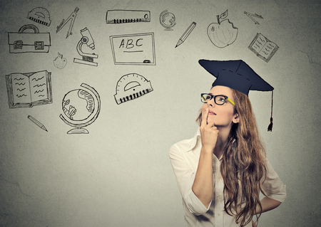 Young beautiful business woman with graduation hat looking up thinking about education isolated on gray wall backgroundの写真素材