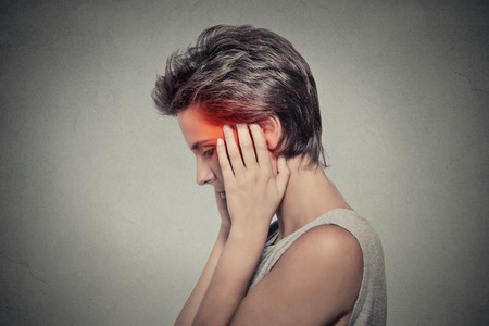 Tinnitus. Closeup up side profile sick female having ear pain headache touching her painful head isolated on gray background. Human face expressionの写真素材