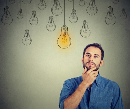 Portrait thinking handsome man looking up with idea light bulb above head isolated on gray wall background