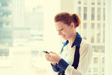 Side profile portrait beautiful young business woman texting on her smart phone isolated on acuity urban backgroundの写真素材