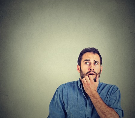 Closeup portrait nervous stressed young man student biting fingernails looking up anxiously craving something isolated on grey wall background. Human emotion face expression feelingの写真素材
