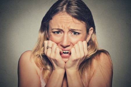 Closeup portrait headshot nervous stressed young woman girl student biting fingernails looking anxiously craving something isolated grey wall background. Human emotion face expression feelingの写真素材