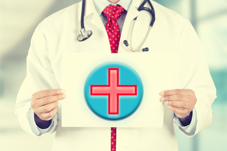 Closeup doctor hands holding white card with First Aid icon isolated on hospital clinic office background.の写真素材