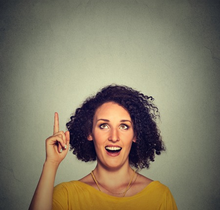 Portrait happy beautiful woman with idea looking up pointing with finger at blank copy space isolated gray background. Positive human face expression emotion feeling body language perceptionの写真素材