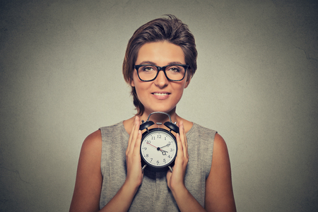 young smiling woman with alarm clock isolated grey wall background. Human face expression. Time, punctuality, busy schedule conceptの写真素材