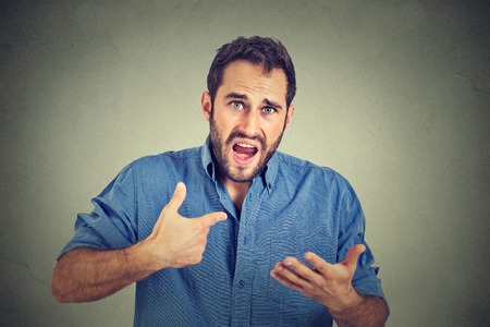 Closeup portrait of angry, mad, unhappy young guy pointing at himself asking you mean me, you talking to me, isolated on gray background. Negative human emotion facial expression feelingの写真素材