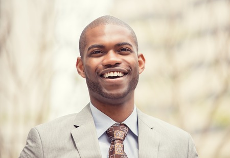 Headshot portrait of young professional man smiling laughing isolated on outside outdoors corporate office background. Positive human emotions feelings facial expressionsの写真素材