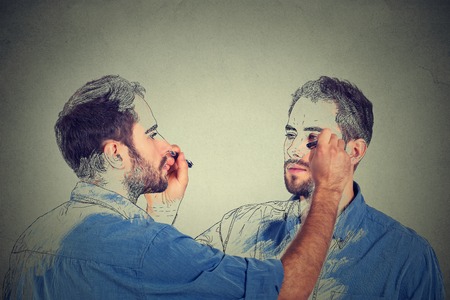 Create yourself concept. Good looking young man drawing a picture, sketch of himself on grey wall background. Human face expressions, creativityの写真素材