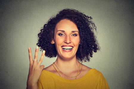 Closeup portrait of young pretty woman giving a three fingers sign gesture with hand isolated on gray wall background. Positive human emotions, facial expressions, feeling, symbols, body languageの写真素材