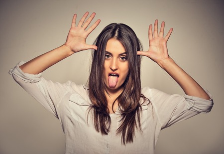 Young pretty woman with funny face mocking someone sticking her tongue out isolated on gray wall backgroundの写真素材