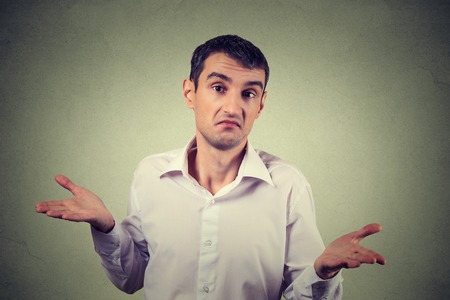Closeup portrait young upset man shrugging shoulders who cares so what I don't know gesture isolated on grey wall background. Body language expression. Man showing ignoranceの写真素材