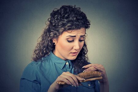 Closeup unhappy frustrated young woman surprised she is losing hair, noticed split ends receding hairline. Gray background. Human face expression emotion. Beauty hairstyle conceptの写真素材