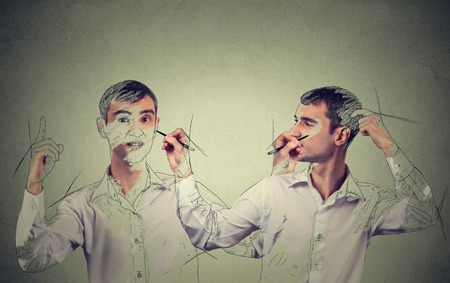 Create yourself concept. Good looking young man drawing a picture, sketch of himself on grey wall background. Human face expressions, creativityの写真素材