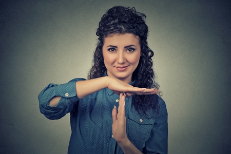 Closeup portrait, young, happy, smiling woman showing time out gesture with hands isolated on gray...