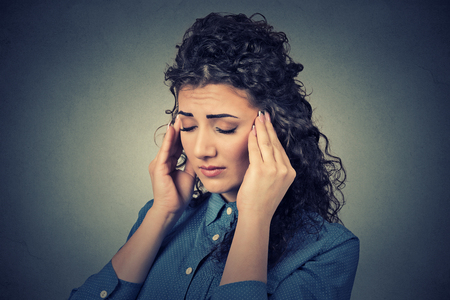 Closeup sad young woman with worried stressed face expression having headache isolated on gray wall background. Human emotions, mental health conceptの写真素材