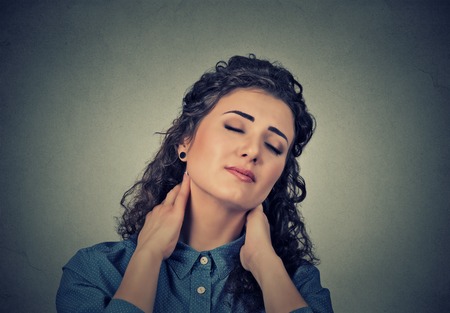 Back and spine disease. Closeup portrait tired woman massaging her painful neck isolated on gray wall background. Human face expression. Chronic fatigue diseaseの写真素材