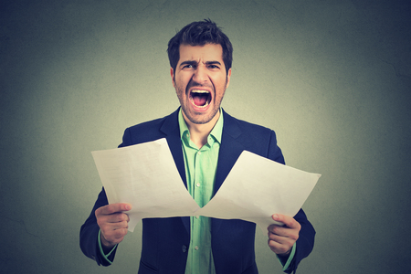 Angry stressed screaming business man with documents papers paperwork isolated on gray office wall background. Negative emotions face expressionの写真素材