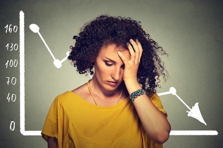 Frustrated stressed sad business woman with financial market chart graphic going down on gray office wall background. Poor economy concept. Face expression, emotion, reactionの写真素材