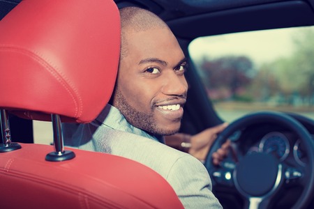 Portrait happy handsome young man in new car hands on wheel, turning around, smiling looking at, talking to passengers sitting in back seat. Driver license exam, test conceptの写真素材