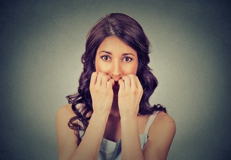 Closeup portrait young unsure hesitant nervous woman biting her fingernails craving for something or anxious isolated on gray wall background. Negative human emotions facial expression feelingの写真素材