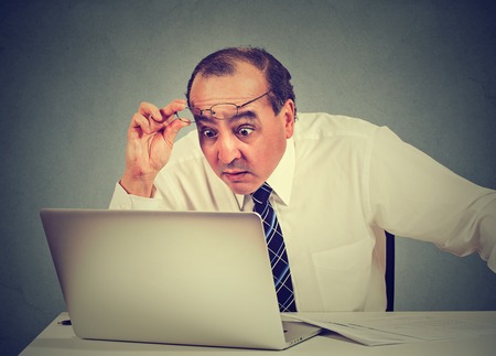 Portrait of a shocked man reading message on computer in officeの写真素材