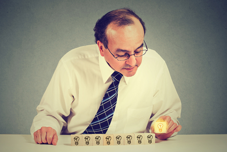Middle aged business man sitting at table desk with yellow bright light bulb idea. Concept of innovation and problem solvingの写真素材