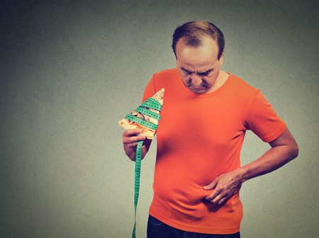 Middle aged man with slice of pizza measuring tape and overweight abdomen. Weight loss dieting conceptの写真素材