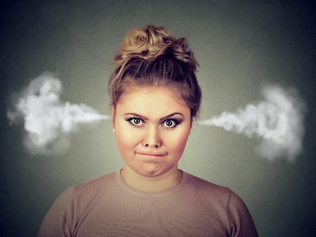 Closeup portrait of angry young woman, blowing steam coming out of ears, about to have nervous atomic breakdown isolated on black background. Negative human emotion facial expression feelings attitudeの写真素材