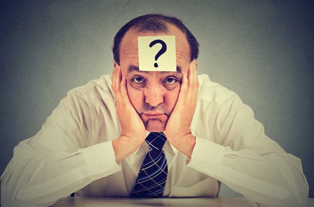 clueless business man with question mark sitting at table isolated on gray wall backgroundの写真素材