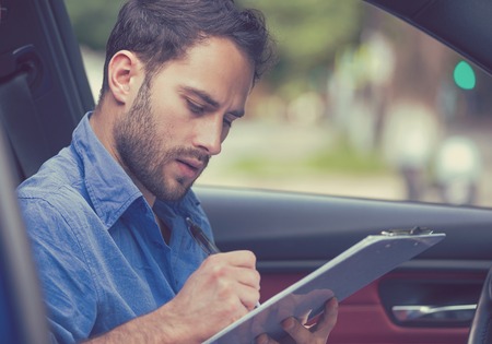 transportation and ownership concept. Young handsome man inside new car reading signing documentsの写真素材