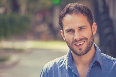 Happy young man. Closeup portrait of handsome guy in casual shirt smiling while standing against city urban backgroundの写真素材