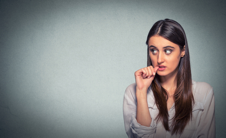 Procrastination. Confused thinking young woman bewildered sucking thumb looking up at isolated on gray wall background. Human face expressionの写真素材