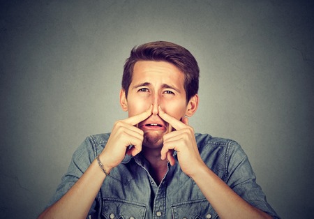 man pinches nose with fingers looks with disgust something stinks bad smell isolated on gray background. Human face expression body language reactionの写真素材
