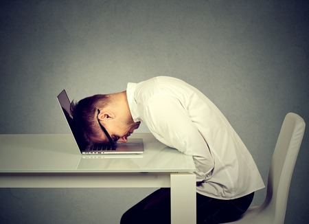 Desperate employee, stressed young man resting head on laptop keyboardの写真素材