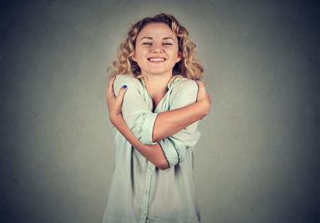 Smiling woman holding hugging herself isolated gray wall background. Positive human emotion, facial expression, feeling, attitude. Love yourself conceptの写真素材