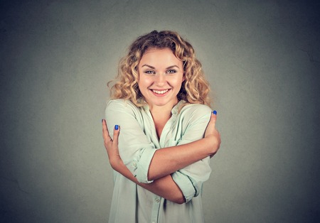 Smiling woman holding hugging herself isolated gray wall background. Positive human emotion, facial expression, feeling, attitude. Love yourself conceptの写真素材
