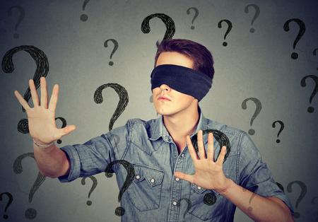 Portrait blindfolded man stretching his arms out walking through many question marks isolated on gray wall backgroundの写真素材
