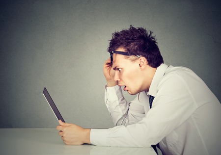 Side profile shocked young man looking at his laptop computer sitting at tableの写真素材