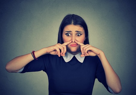 Closeup portrait woman pinches nose with fingers looks with disgust something stinks bad smell isolated on gray wall background. Human face expression body language reactionの写真素材
