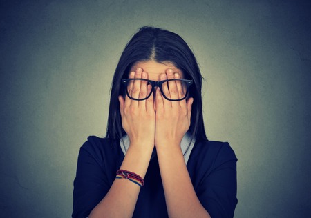 Closeup portrait young woman in glasses covering face eyes using her both hands isolated on gray wall backgroundの写真素材